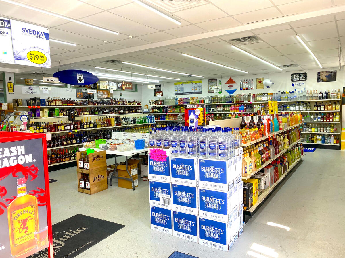 Port City Two Liquors and Wine – Extensive Premium Spirits & Wine Aisles A wide-angle interior view of Port City Two Liquors and Wine showing long, well-organized aisles of vodka, gin, rum, and cognac. The store features bright overhead lighting, clean wood-style flooring, and rustic wooden barrel displays near the checkout cou
